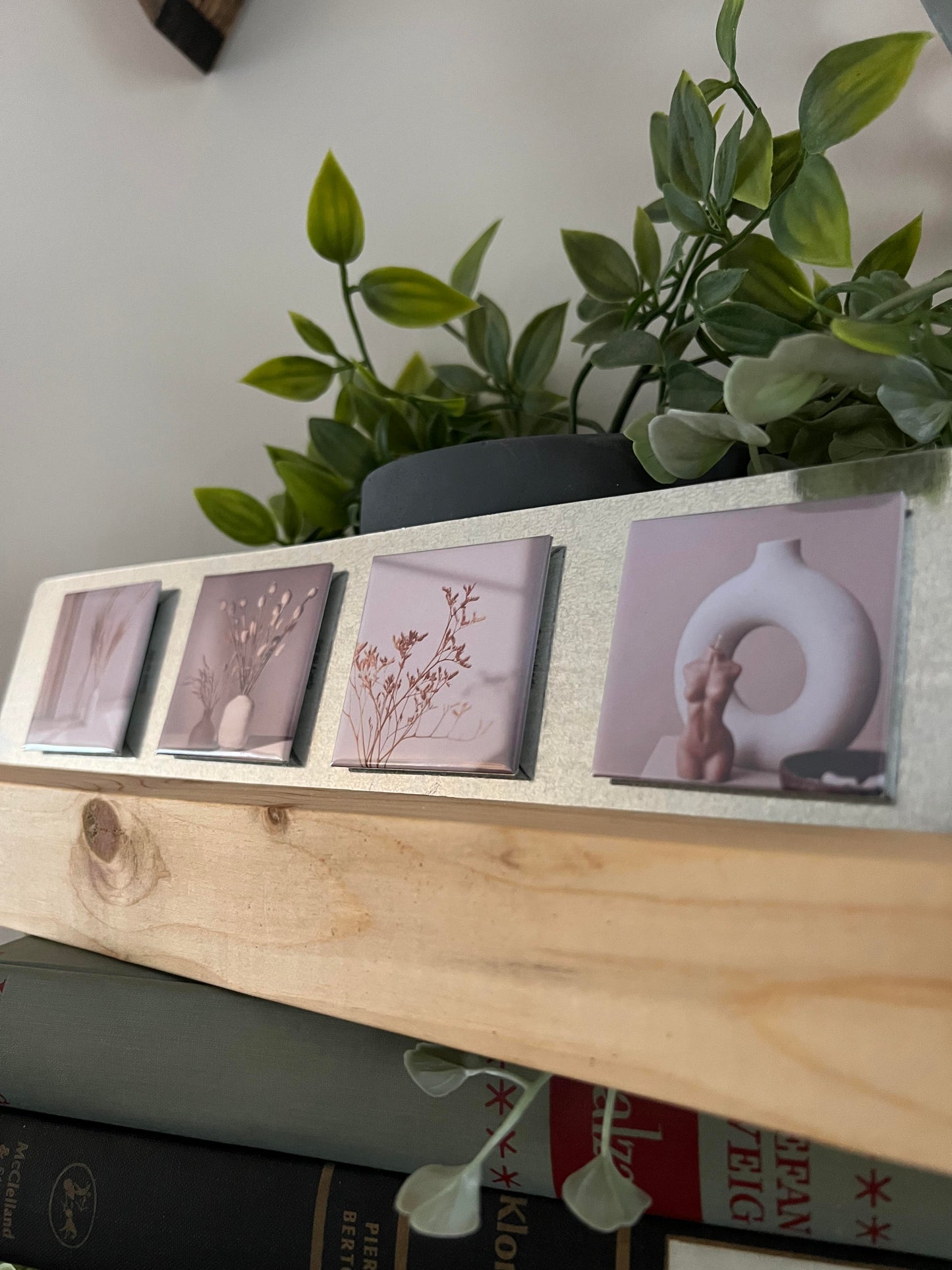 Wooden stand with photo magents with floral images on a surface with books and a plant.