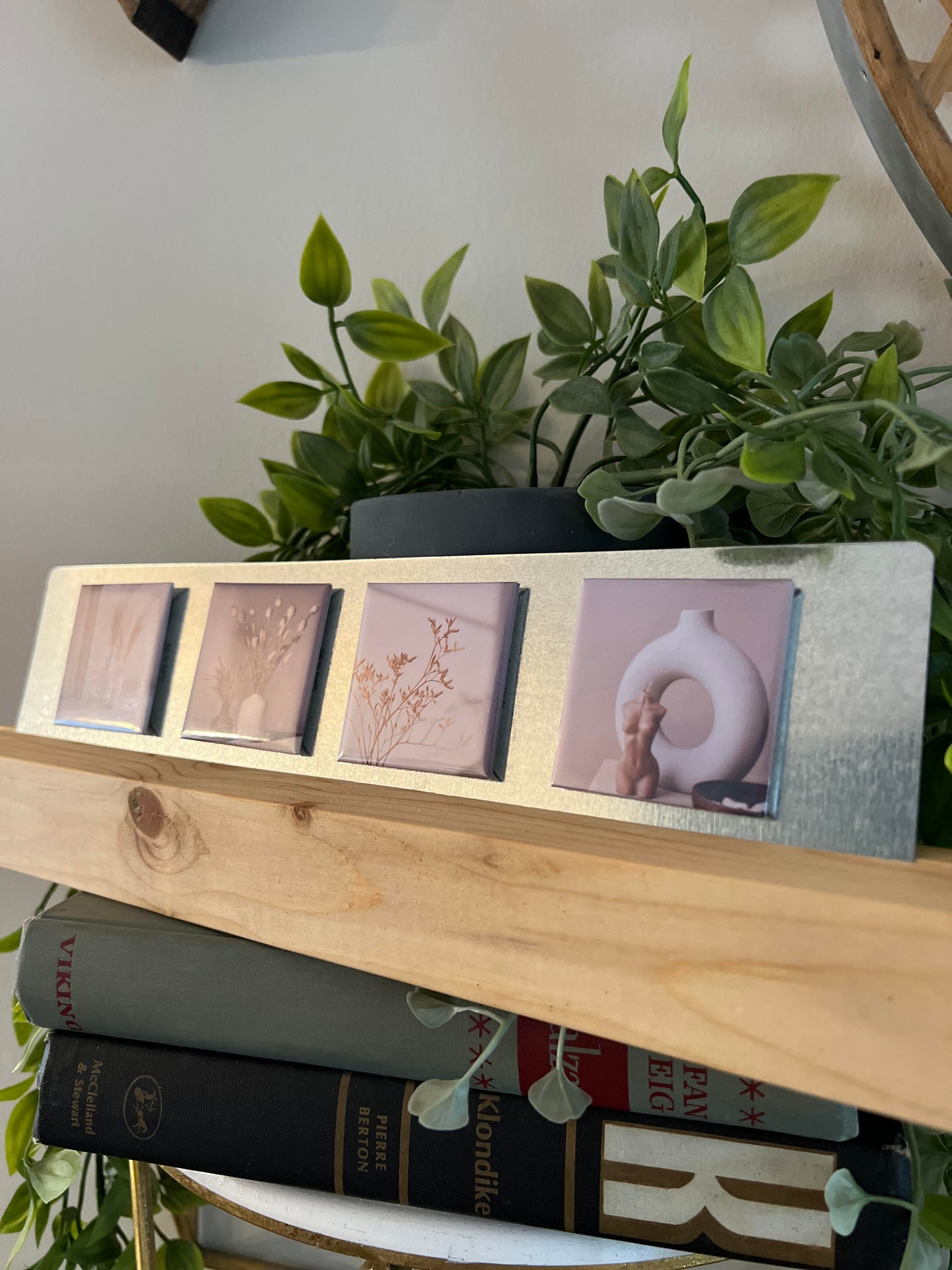 Wooden photo stand with photo magnets on top of books, surrounded by green plants. neutral, beige white aesthetic, decorations