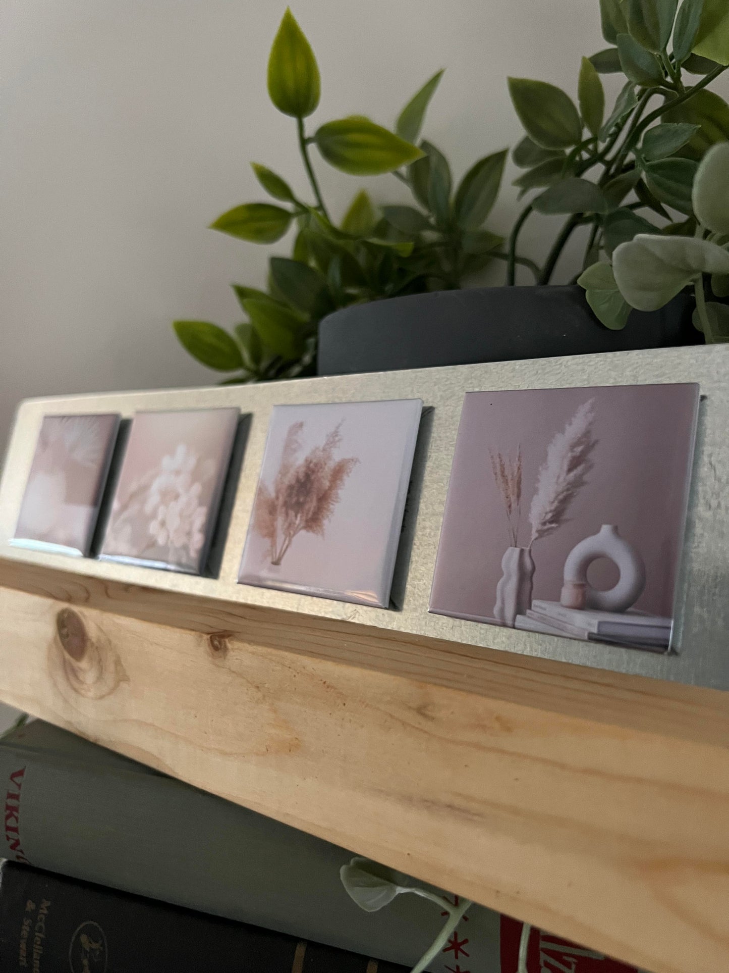 Wooden block with four small artworks turned into magnets of aesthetic styles on a surface with plants in the background