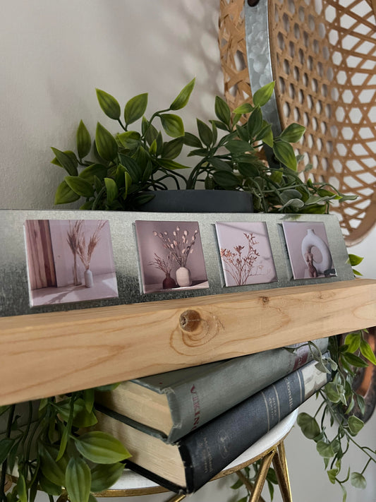 Stack of books with a photo stand and neutral magnets on top, surrounded by green plants.