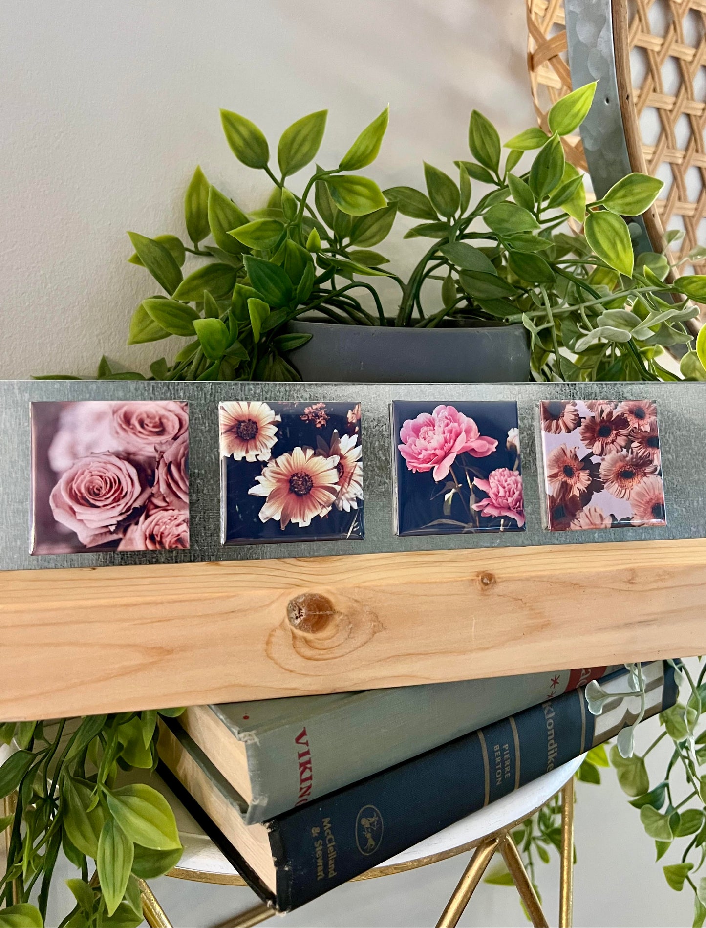Decorative photo stand with magnets displayingwith floral designs on a shelf with books and plants.
